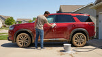 Man washing a muddy red SUV car rental in a driveway to clean the vehicle after an off-road adventure.